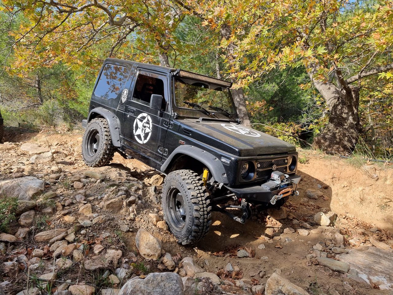 A robust 4x4 vehicle tackling rough terrain in a wooded outdoor setting, ideal for adventure enthusiasts.