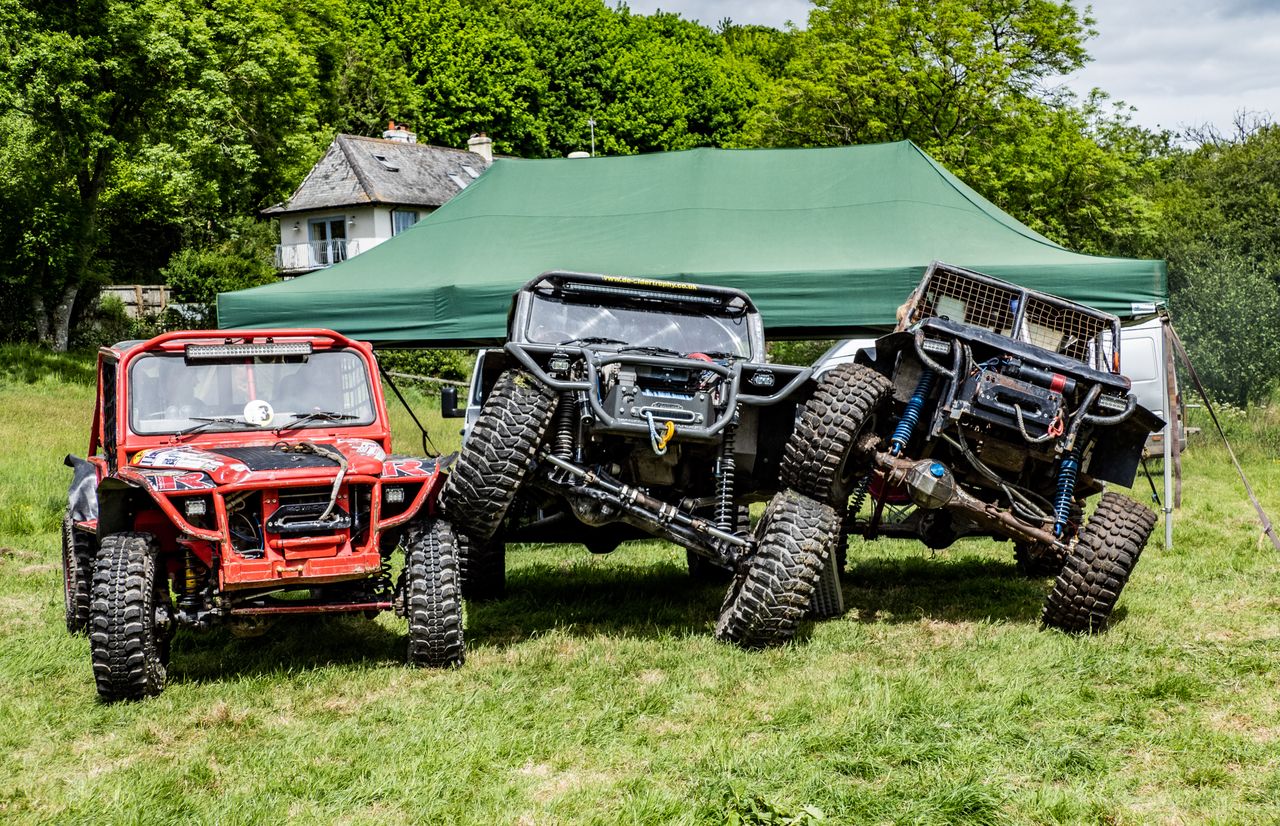 Three rugged off-road vehicles parked under a green tent on a grassy field during the day.