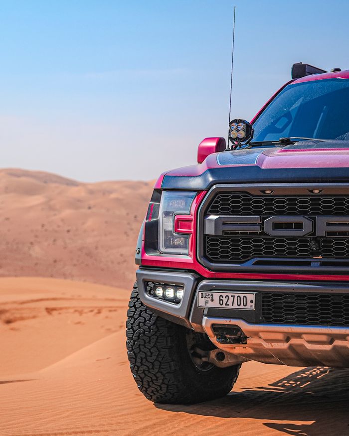 Red pickup truck on Dubai sand dunes under clear blue sky.